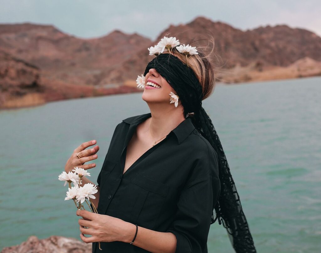 Mastering the First Impression: Your intriguing post title goes here A joyful woman with a floral blindfold enjoying nature by a serene lake and rocky landscape.